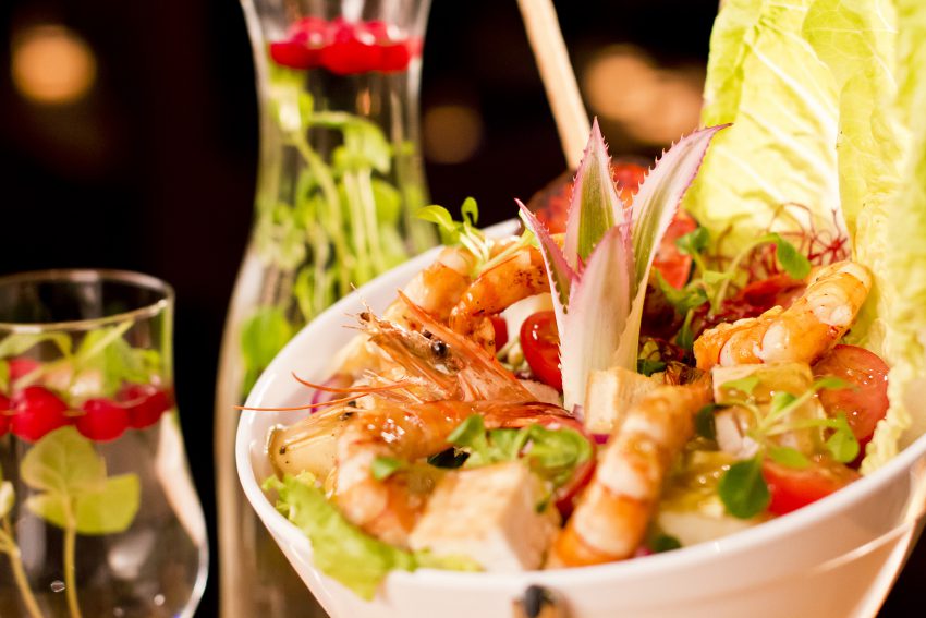 Seafood salad with shrimps in white bowl on black background